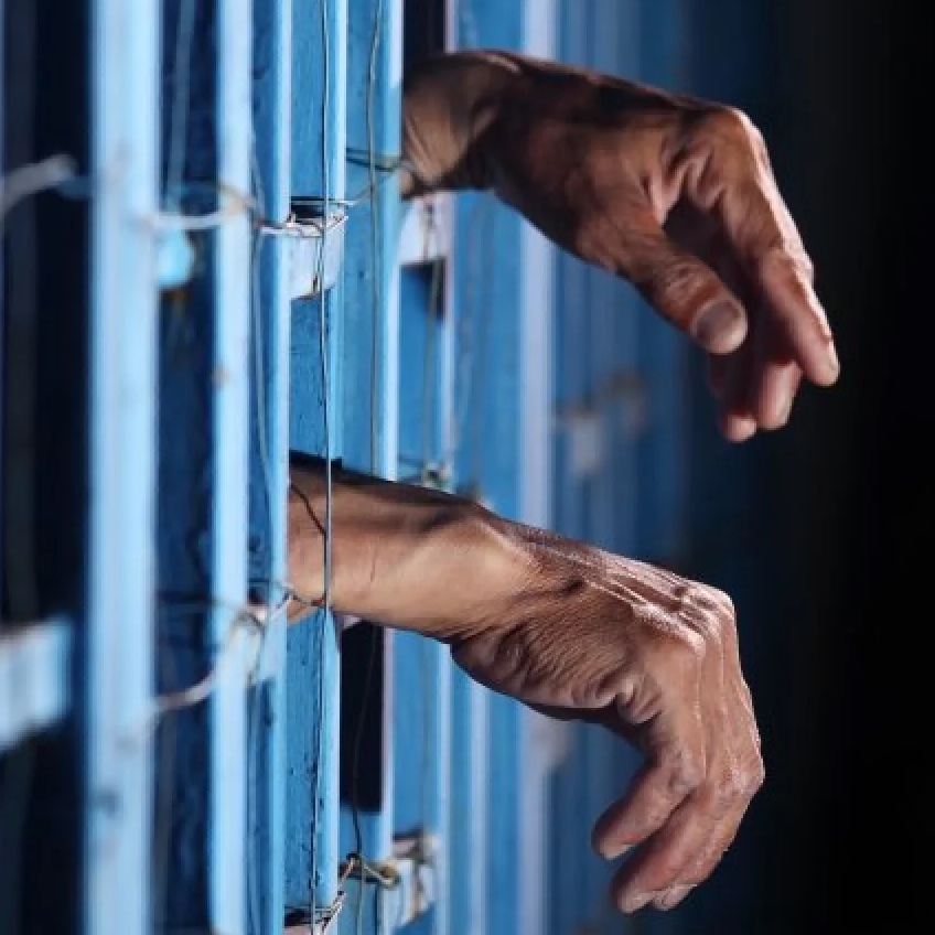 Man sticking his hands between prison bars