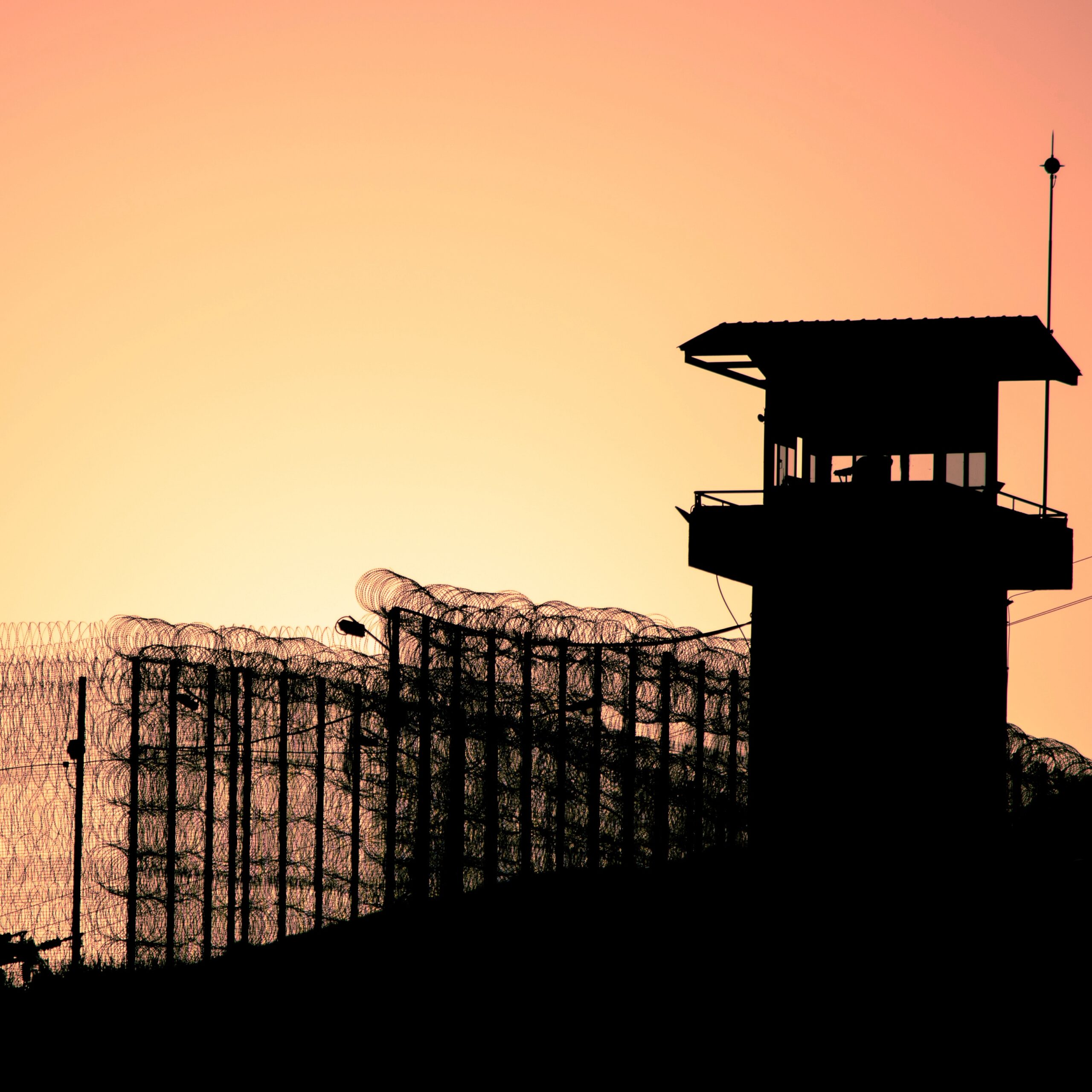 Silhouette of barbed wires and watchtower of prison in Neapolis, Crete, at sunset