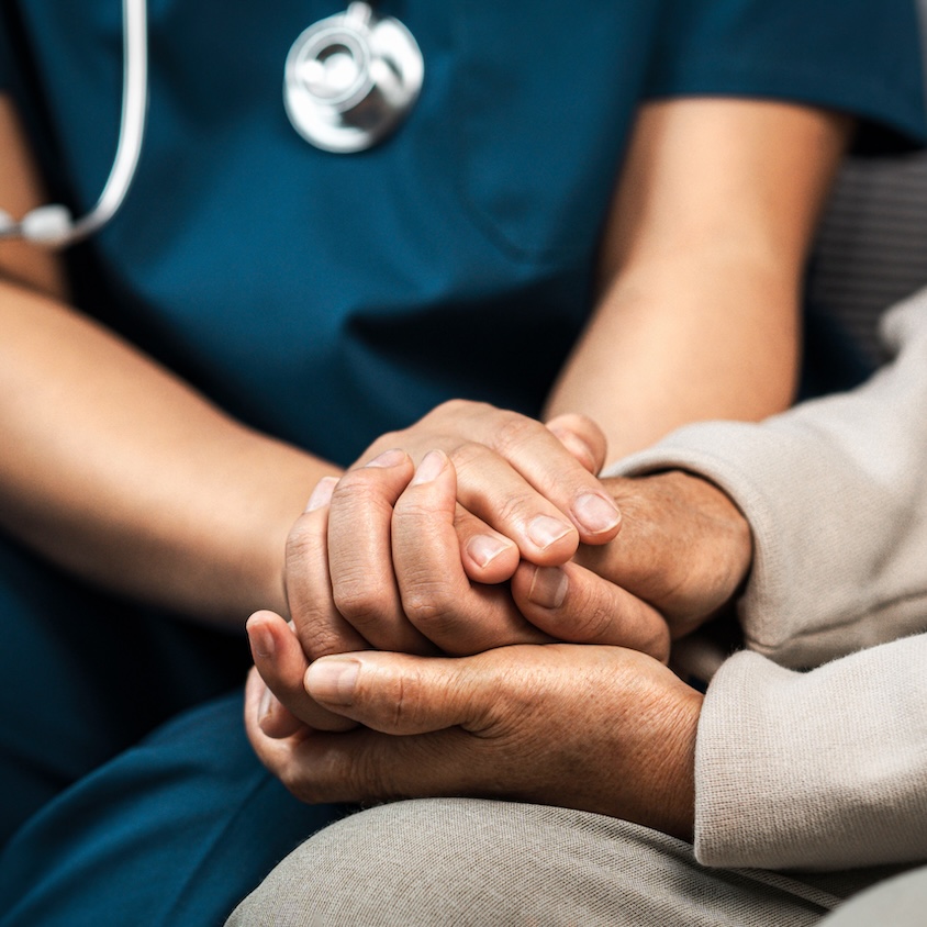 A female nurse caregiver holds hands to encourage and comfort a woman.