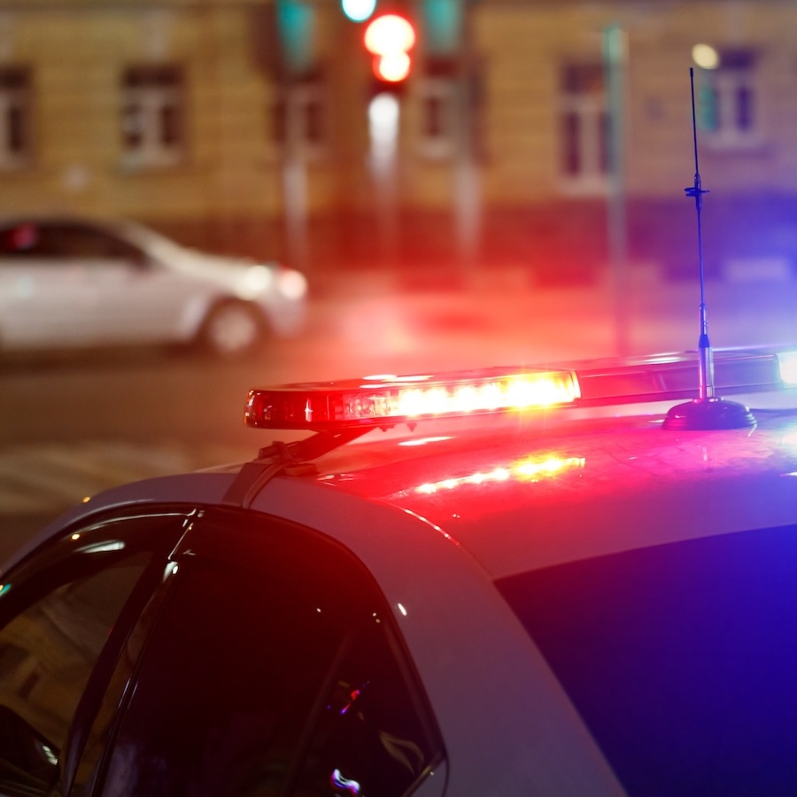 Police car lights in street with civilian car in blurry background at night, fear of crime